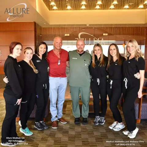 A group of eight people, including two men and six women, stand together in professional attire inside a medical aesthetics and wellness clinic named Allure Medical.